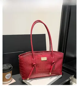 Détail du sac cabas rouge motif crocodile avec poignée nouée et breloque logo en métal doré