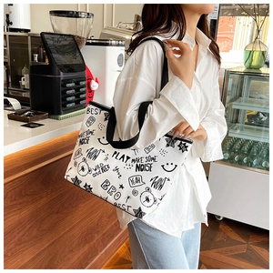 Detail of white canvas tote bag with black graffiti prints worn by a model in a cafe