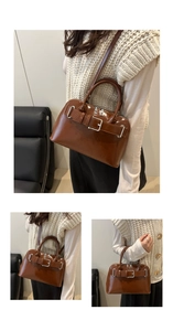 Detail view of glossy dark brown handbag featuring decorative belt buckle and top handles