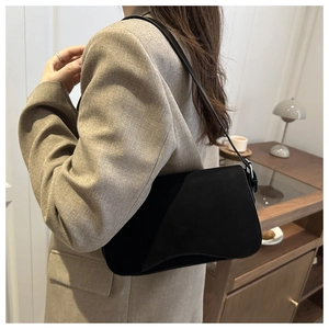 Detail of minimalist black shoulder bag with curved base shown in a lifestyle scene