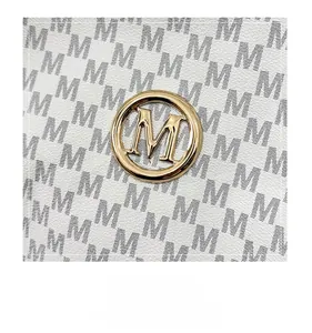 Detail of golden metal M logo on white faux leather tote with black monogram print