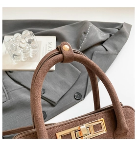 Detail of premium brown matte leather handbag featuring gold clasp and handle hardware