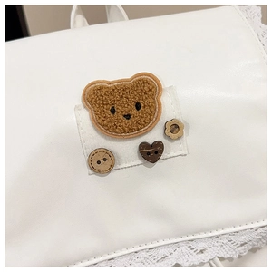 Close-up of white leather backpack with bear patch, buttons and lace edge detail