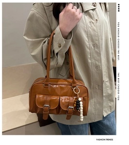 Dettaglio di una borsa tote in vernice marrone con tasche con fibbia e ciondolo a sfere