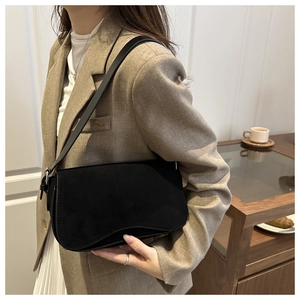 Detail of minimalist black suede shoulder bag with magnetic flap and slim strap