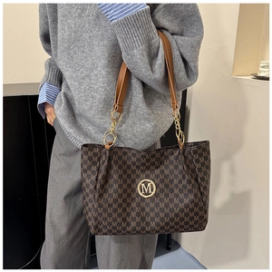 Detail of dark brown tote bag with M-pattern print and gold chain strap on grey knit sweater