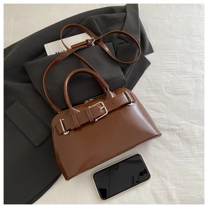 Close-up of caramel brown glossy shoulder bag with buckle detail on white fabric