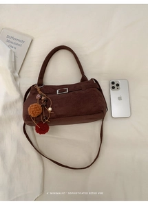 Detail of dark brown suede handbag with decorative retro pompom charm and metal buckle