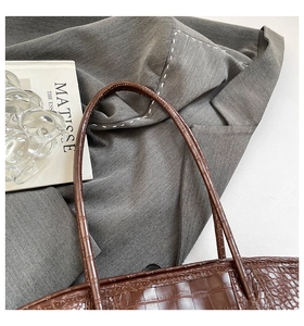 Gros plan sur la texture crocodile et les poignées d'un grand sac cabas marron foncé