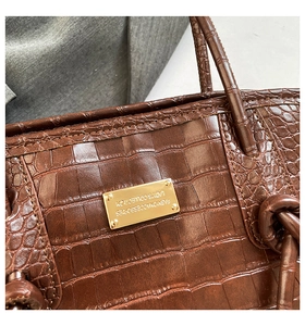 Détail de la texture crocodile marron foncé et plaque dorée sur le sac fourre-tout