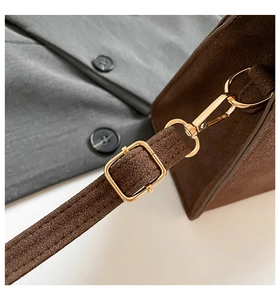 Detail of brown suede handbag featuring an adjustable strap and gold metal buckle
