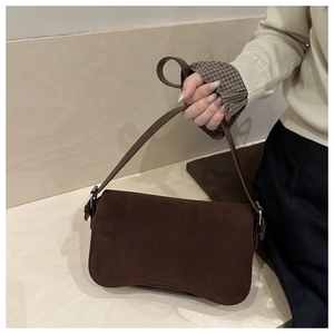 Close-up of a vintage dark brown matte suede underarm bag held by a model in a minimalist setting