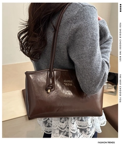 Detail of dark brown glossy shoulder bag with gold lettering shown on a model