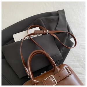 Detail of a brown glossy PU leather handbag with cylindrical handles and metal buckle accent