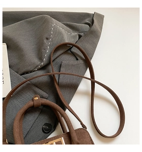 Detail of matte brown crossbody bag with metal buckle on grey suit jacket background