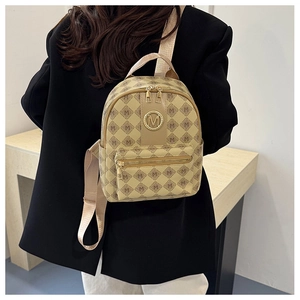 Détail d'un mini sac à dos à motif M beige et marron porté sur une veste noire par un mannequin