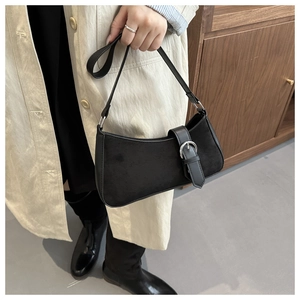 Detail of a black suede hobo bag with silver buckle and leather strap held by a model