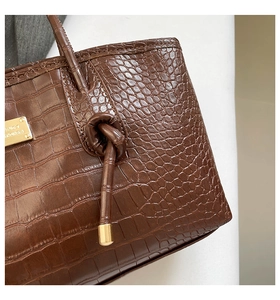 Détail du cuir marron foncé à motif crocodile avec logo en métal doré et poignée nouée chic