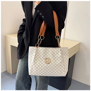 Detail of a white tote bag with grey M pattern, gold hardware and brown shoulder strap