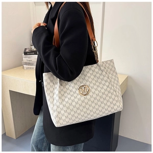 Detail of a large white tote bag with M-pattern print and gold circular metal logo