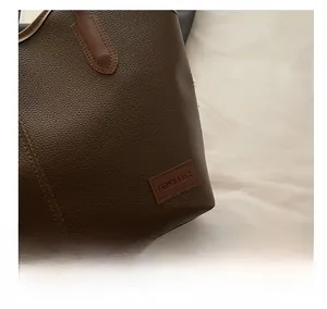 Detailed close-up of dark brown lychee-patterned faux leather tote bag with logo patch