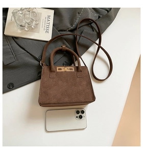 Detail view of brown matte suede small tote bag with golden buckle and phone for scale