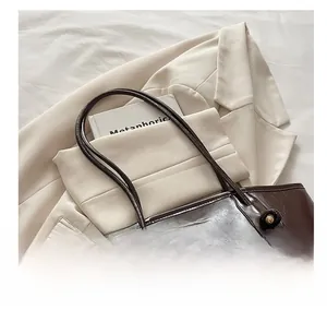 Detail of chocolate brown leather tote bag with metal logo on a stylish blazer background