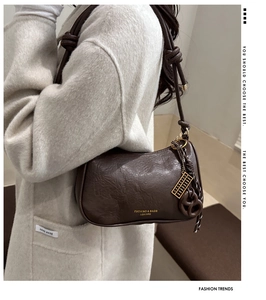 Detail of coffee leather shoulder bag with braided strap and golden abacus charm pendant