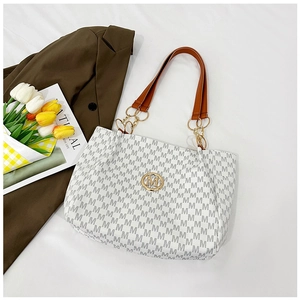 Detail of a white tote bag with M-pattern print and a golden metallic logo ornament