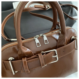 Detail of a brown glossy leather handbag showing silver buckle and fine stitching craft