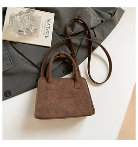 Detail of dark brown matte suede handbag with fine stitching and cylindrical top handle