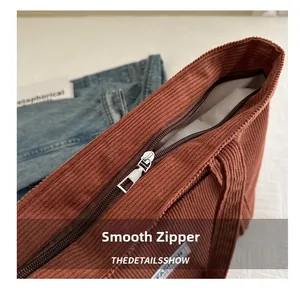 Detailed close-up of smooth metal zipper and corduroy texture on red-brown tote bag