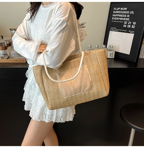 Detail of hand-woven straw tote bag featuring white rope straps and a decorative front pocket
