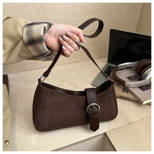 Detail of dark brown suede crescent bag with buckle strap on a light wood desk