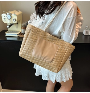 Detail of woven straw tote bag featuring a leather front pocket and slim shoulder straps