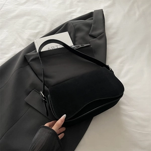 Minimalist black matte suede underarm bag with silver hardware on white fabric