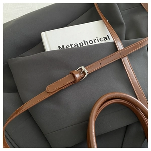 Detailed macro view of the brown leather shoulder strap with a silver buckle and handle