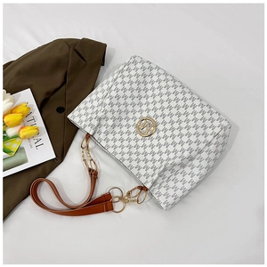 Detail of grey patterned tote bag with golden M logo and brown leather strap on blazer