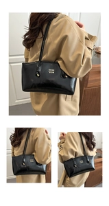 Detail of a large black glossy leather tote bag with gold logo on a trench coat