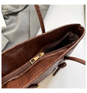 Détail de la texture en cuir gaufré crocodile et de la fermeture éclair dorée du sac
