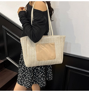 Detail view of cream woven tote bag with brown leather patch and slim shoulder straps
