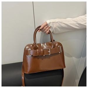 Macro shot of dark brown glossy patent leather shell bag with buckle detail and zipper