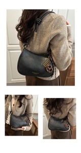 Close-up of black crescent shoulder bag with gold logo and knotted strap detail