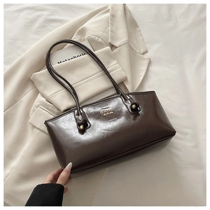 Detail of dark brown glossy leather tote with gold logo on cream blazer background