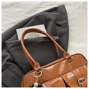 Detail view of the brown leather handbag featuring dual front pockets and metal buckle hardware