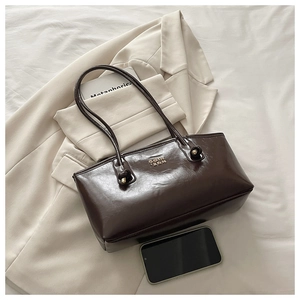Detail of dark brown leather underarm bag with metal logo and shoulder strap knots