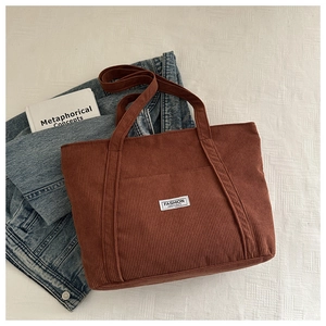 Detailed view of caramel brown corduroy tote bag with white fashion instinct woven label