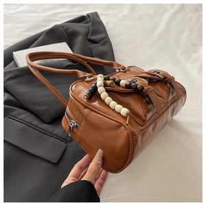 Detail of caramel faux leather Boston bag with decorative straps and beaded charm pendant
