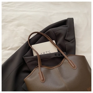 Detail of dark brown tote bag with lychee grain texture and minimalist leather logo patch