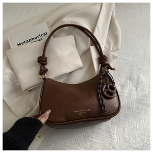 Detail of a dark brown vintage shoulder bag with knot strap on a white blazer background